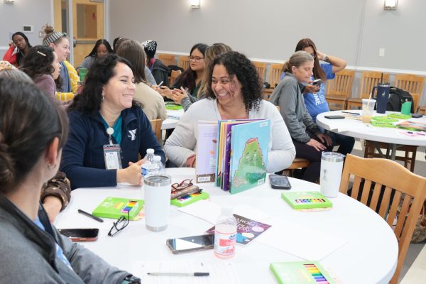 Teachers sitting at a table laughing with books and supplies at tables